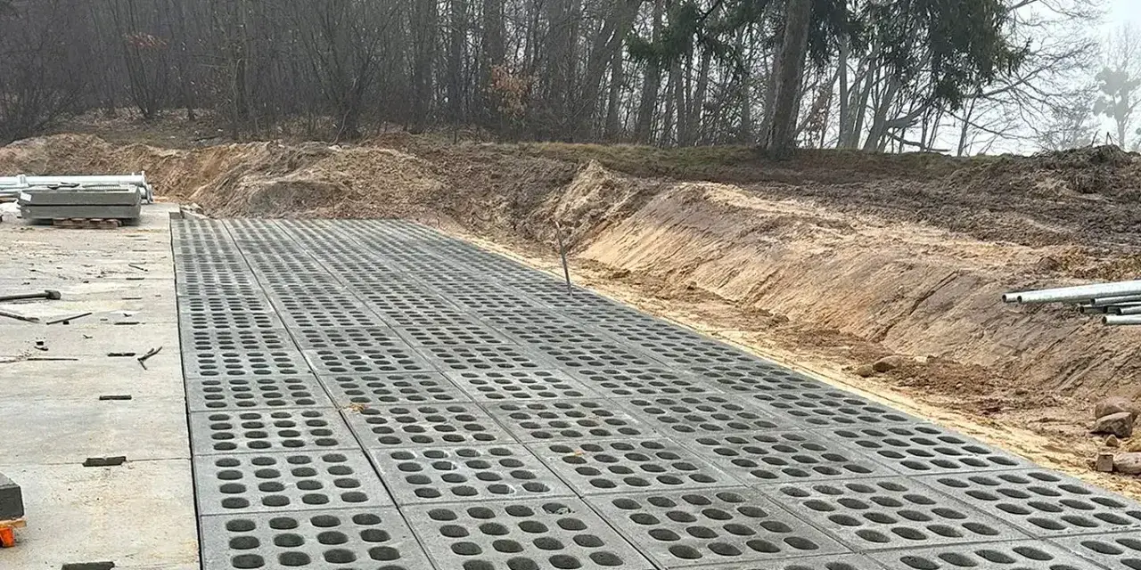 Trwa utwardzenie terenu. Betonowe płyty z otworami tworzą nawierzchnię obok placu budowy z materiałami.