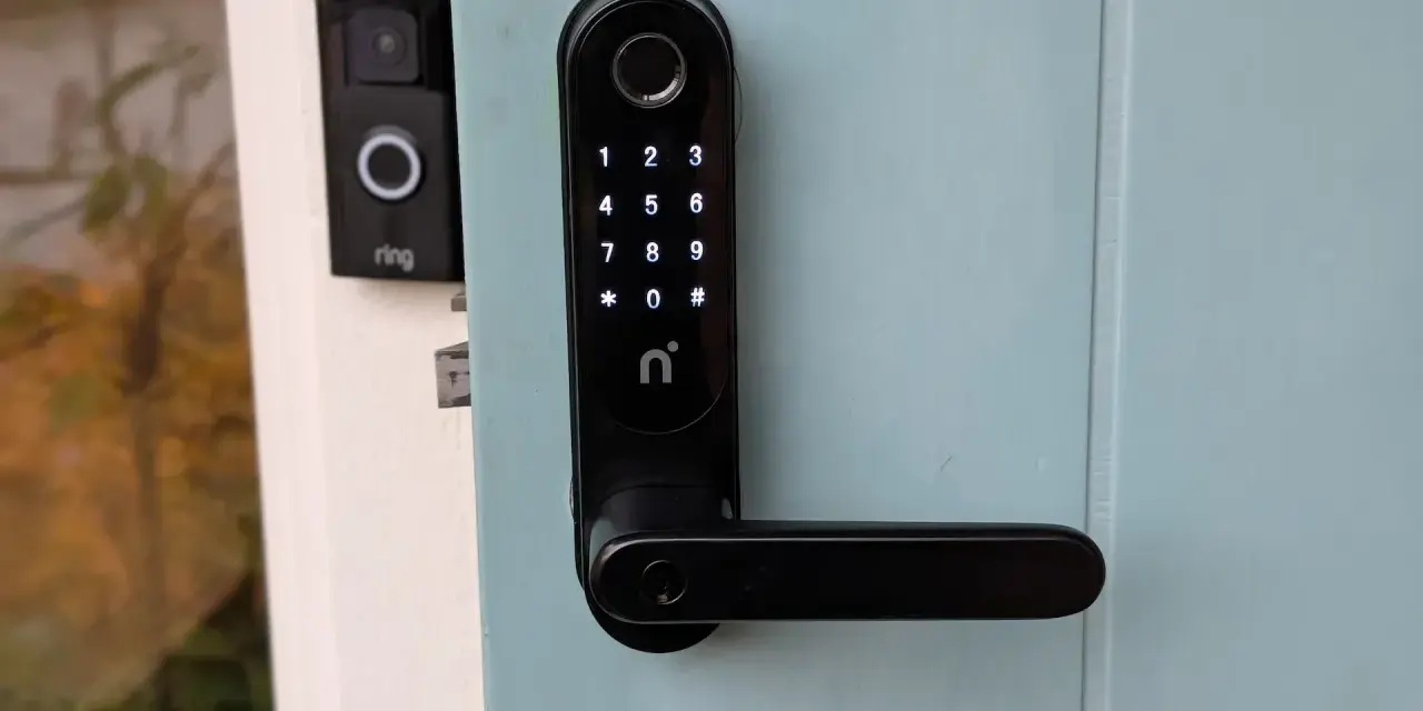 Nimly Touch Pro test: Svart digital dörrlås med kodpanel och fingeravtrycksläsare monterat på en ljusblå dörr. Bredvid syns en Ring-ringklocka.