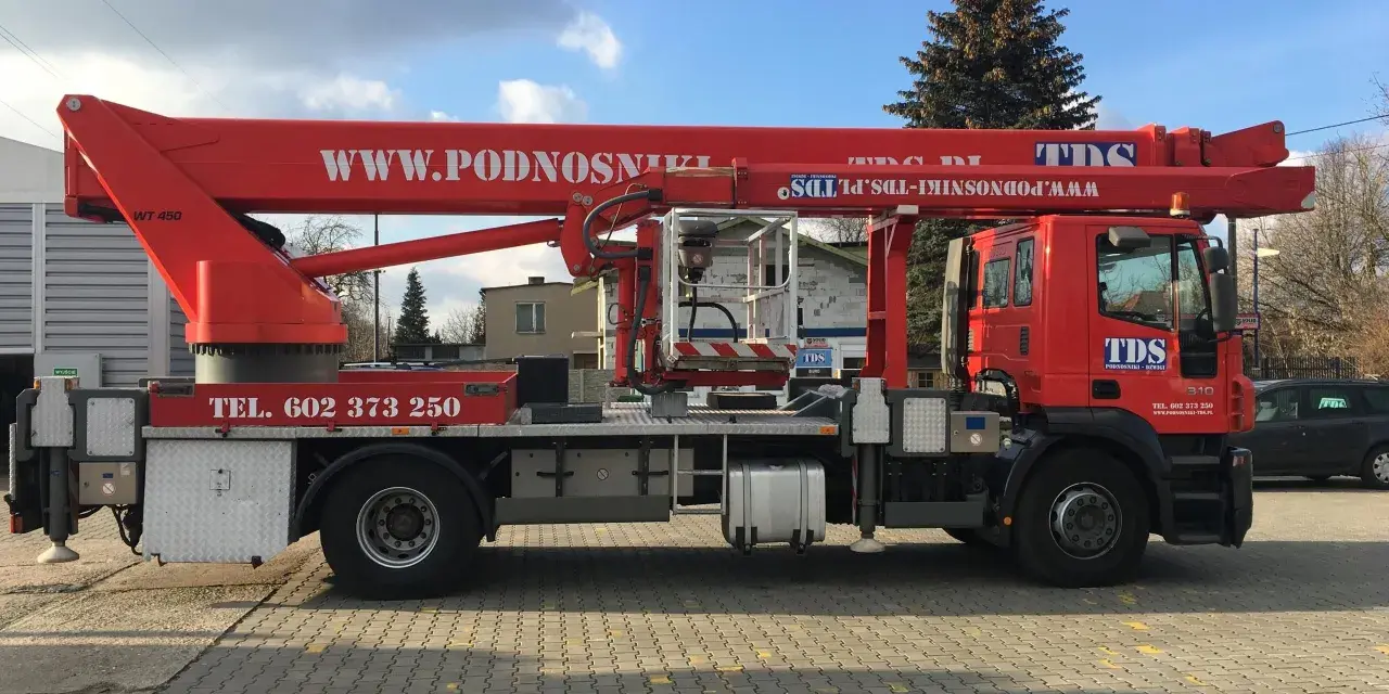 Czerwony podnośnik koszowy WUMAG WT 450 z koszem roboczym i wysięgnikiem. Na pojeździe widnieje napis WWW.PODNOSNIKI-TDS.PL.