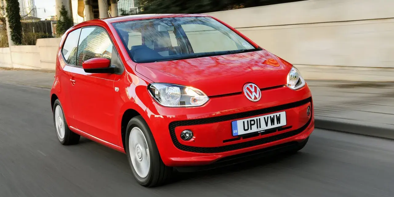 Czerwony Volkswagen up! pędzi po miejskiej drodze, odbijając światła miasta w swojej lśniącej karoserii.