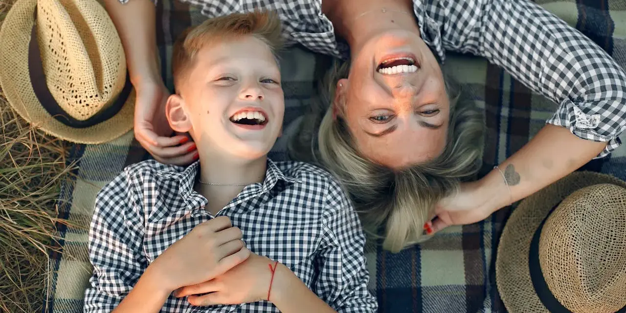 Uśmiechnięta mama i syn leżą na kocu. Idealny dzień na życzenia z okazji Dnia Mamy.