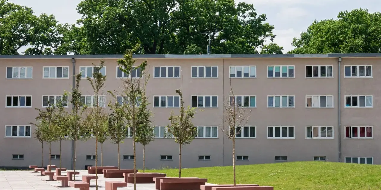Nowoczesny budynek mieszkalny w stylu wuwa Wrocław z rzędem drzew i betonowych ławek przed fasadą.