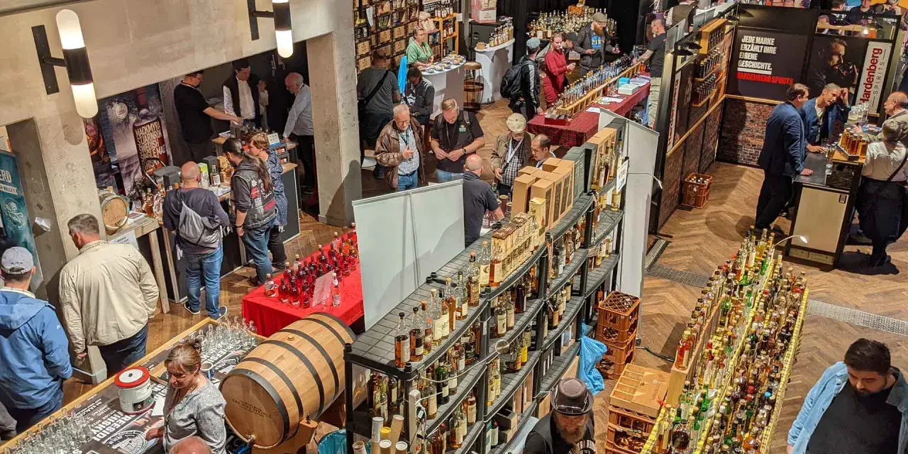 Besucher auf einer Messe probieren Spree-side Whisky. Viele Flaschen und ein Fass sind ausgestellt.