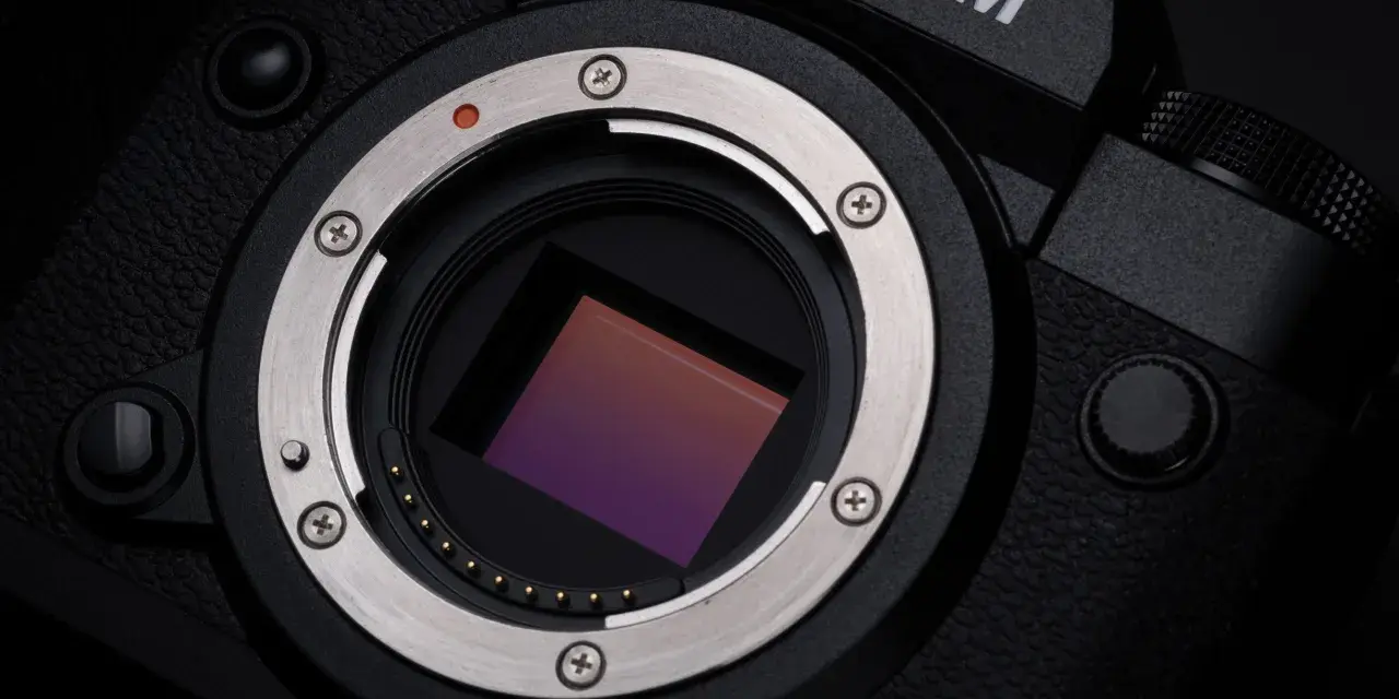 Zbliżenie na matrycę aparatu Fujifilm xh2s, lśniący metalowy pierścień mocowania obiektywu i czerwona kropka sygnalizująca montaż.