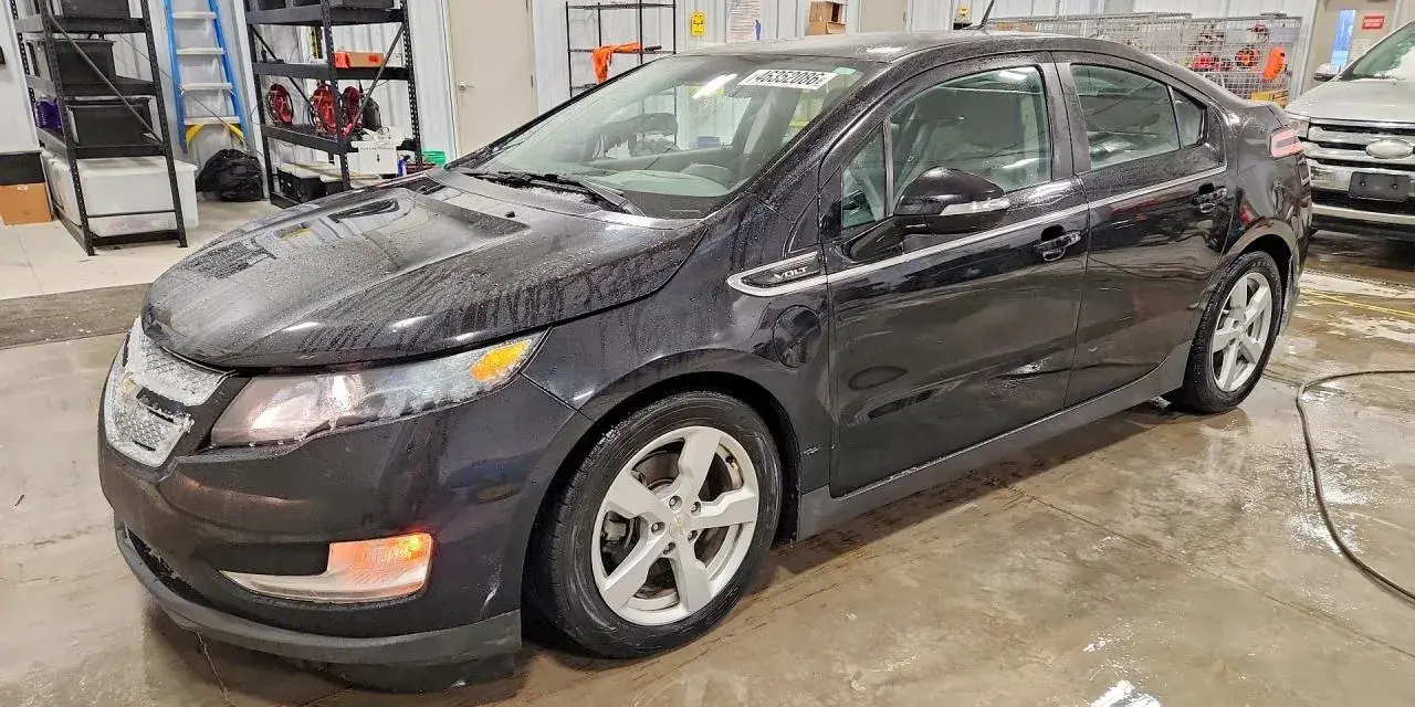 Czarny Chevrolet Volt stoi w garażu, mokry od deszczu. W tle regały z narzędziami i drabina.
