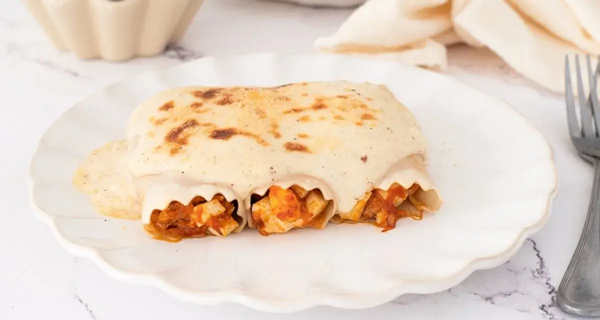 Canelones de atún gratinados con bechamel cremosa, listos para disfrutar en un plato blanco con borde ondulado.