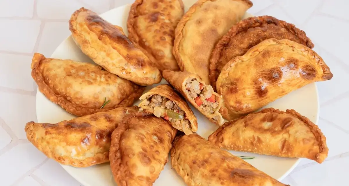 Empanadas de carne doradas y crujientes en un plato, una partida muestra el relleno.