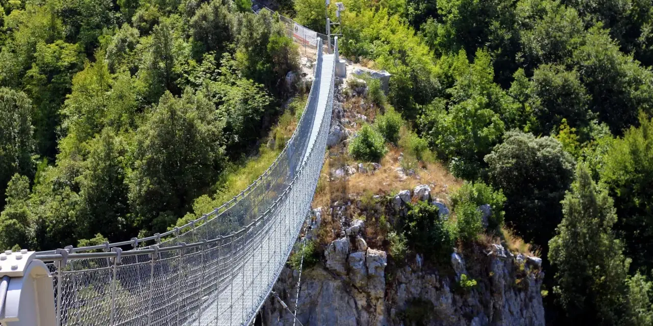 Un avventuroso percorso ponte tibetano si snoda tra rocce e fitta vegetazione, offrendo una vista mozzafiato sulla valle.