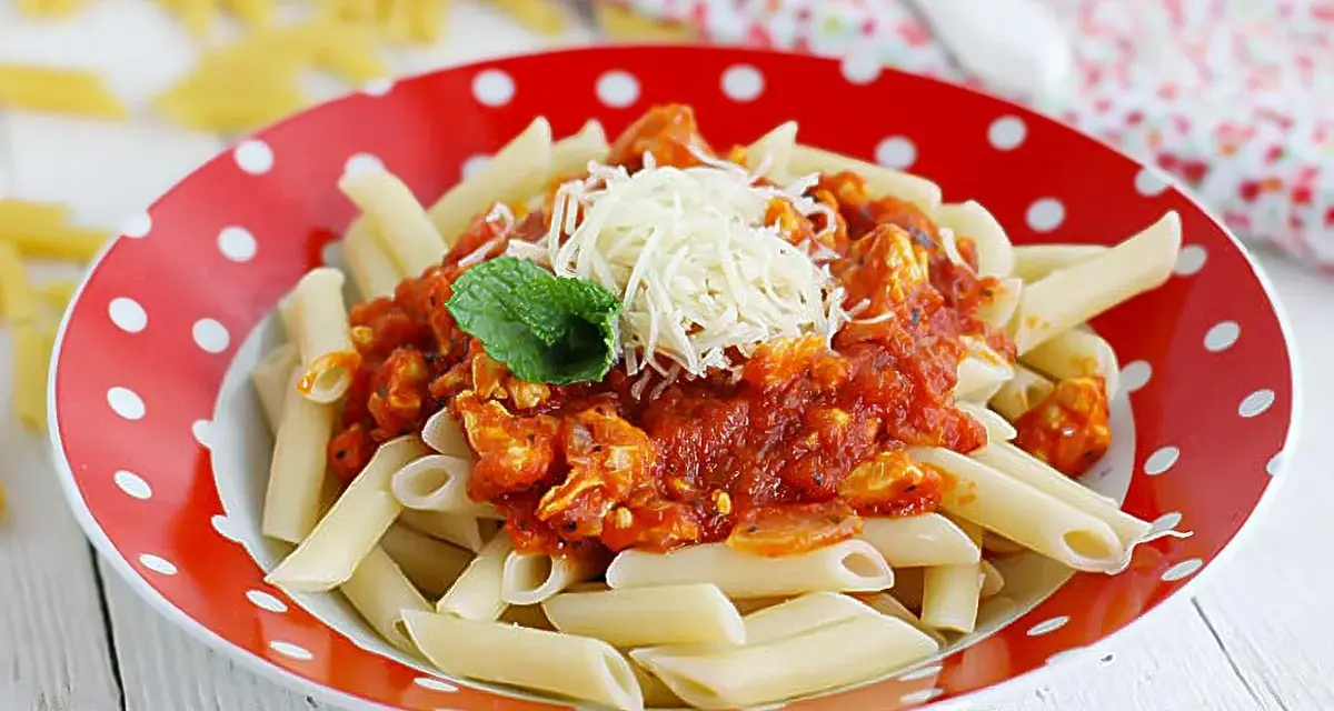 Macarrones con pollo en salsa roja, gratinados con queso y decorados con menta. Un plato delicioso y fácil de preparar.