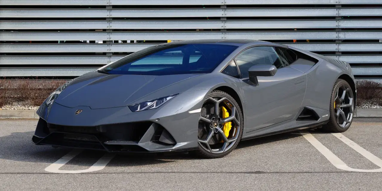 Szary Lamborghini Huracan z żółtymi zaciskami hamulcowymi na tle metalowej ściany.