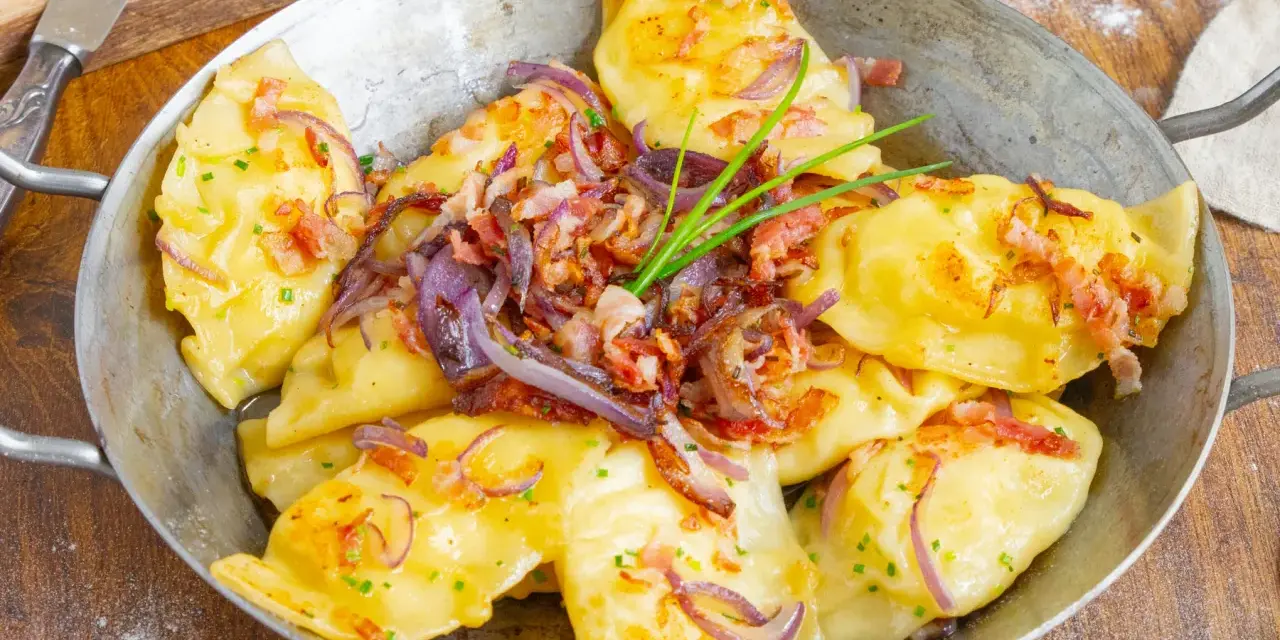 Herzhafte pierogi ruskie, goldgelb und dampfend, garniert mit knusprigem Speck, karamellisierten Zwiebeln und frischem Schnittlauch.