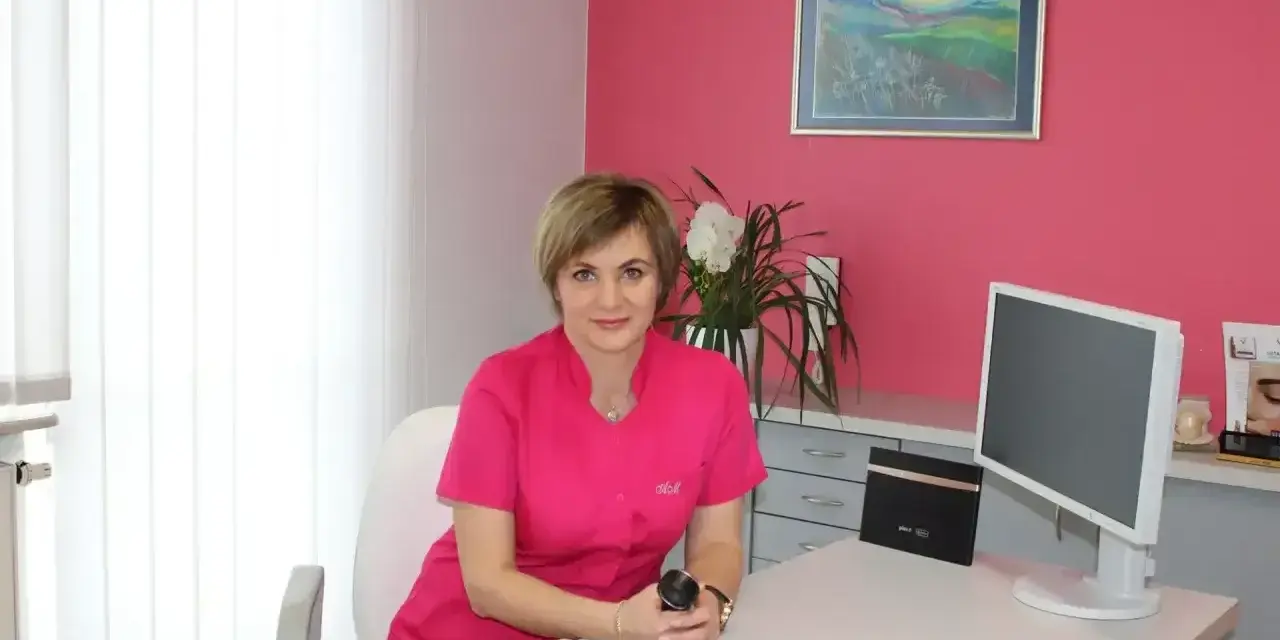 Lekarka w różowym uniformie siedzi przy biurku w gabinecie estetycznym.