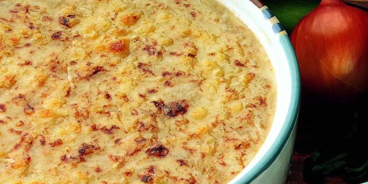Una ricca zuppa di cipolle gratinata, con crostini dorati e formaggio fuso. Accanto, una cipolla rossa e foglie verdi.