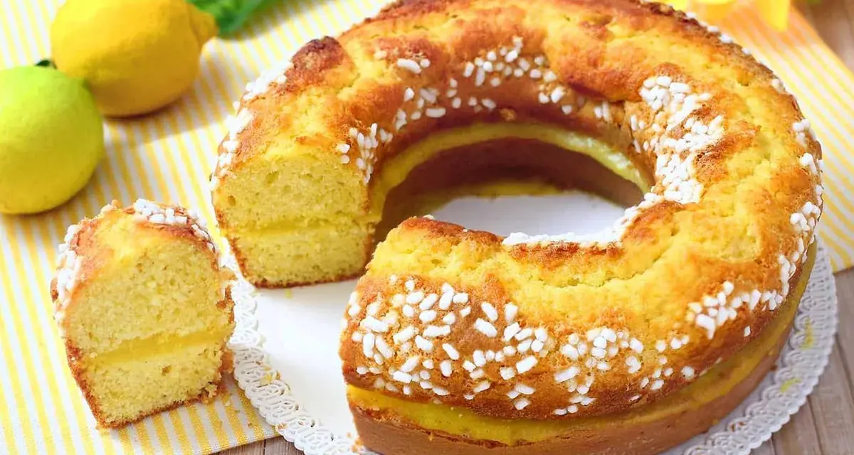 Un soffice ciambellone al limone, con una golosa crema gialla all'interno e decorato con perline di zucchero. Perfetto per la colazione o la merenda.