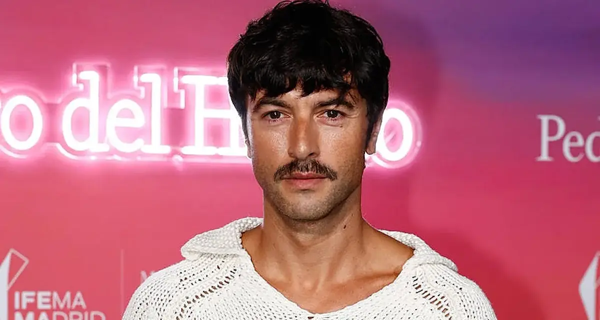 Hombre con un estiloso bigote, perfecto para Movember, luce un jersey blanco de punto.