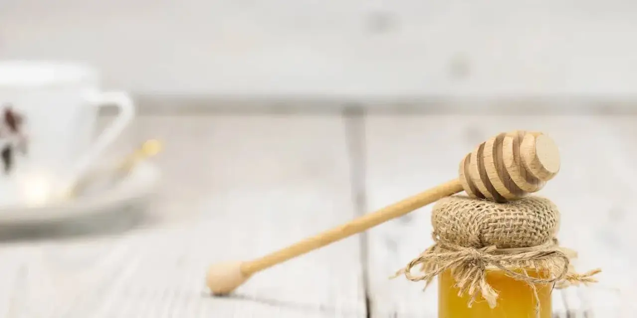 Mały słoiczek miodu z drewnianą chochlą, idealny do herbaty. Warto pamiętać o jego miód kcal.