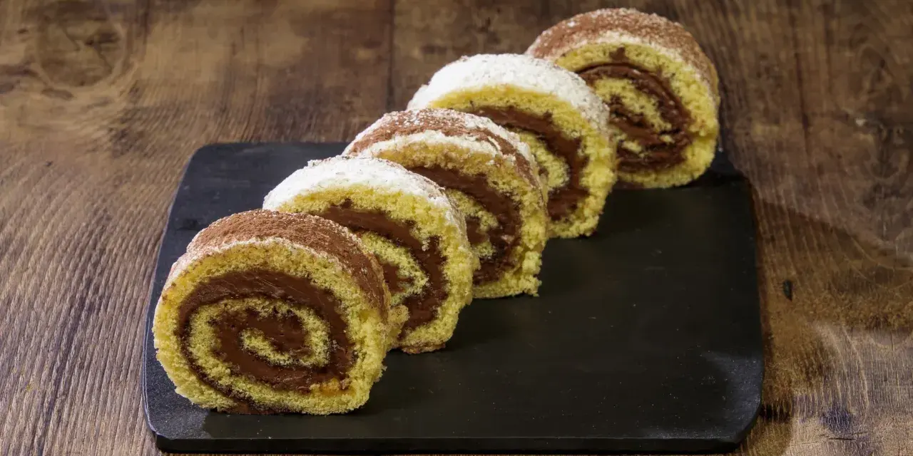 Fette di rotolo alla nutella cosparse di zucchero a velo e cacao, su una lavagna scura, pronte per essere gustate.