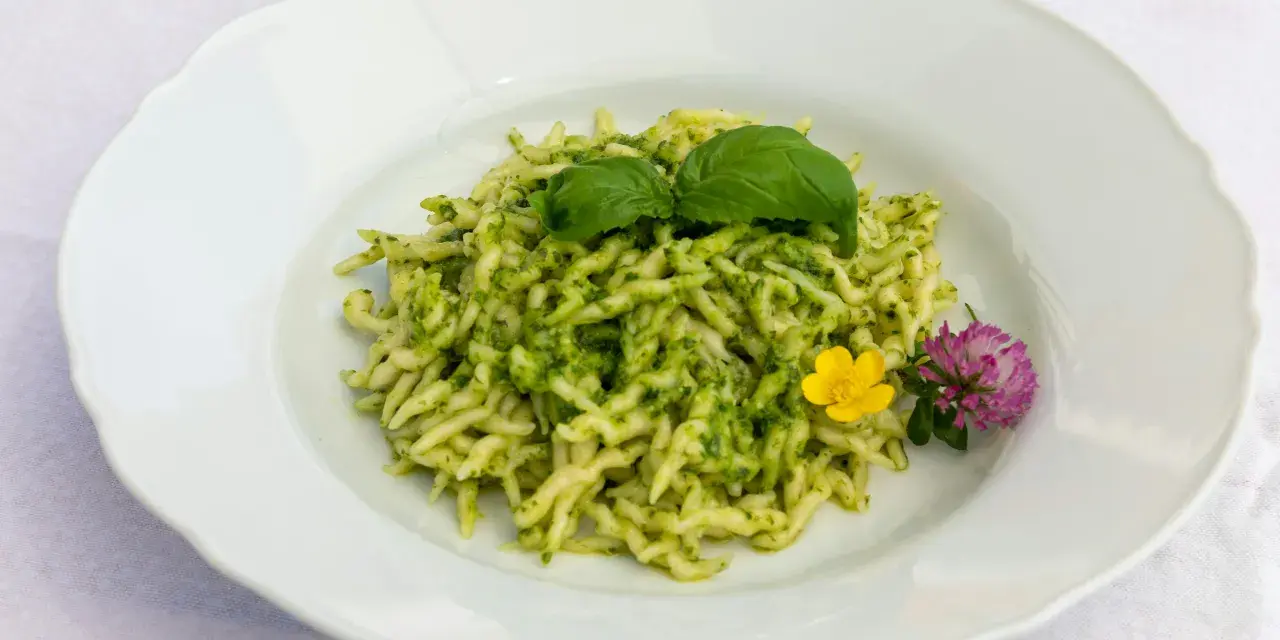 Pasta al pesto con hojas de albahaca fresca y flores comestibles.