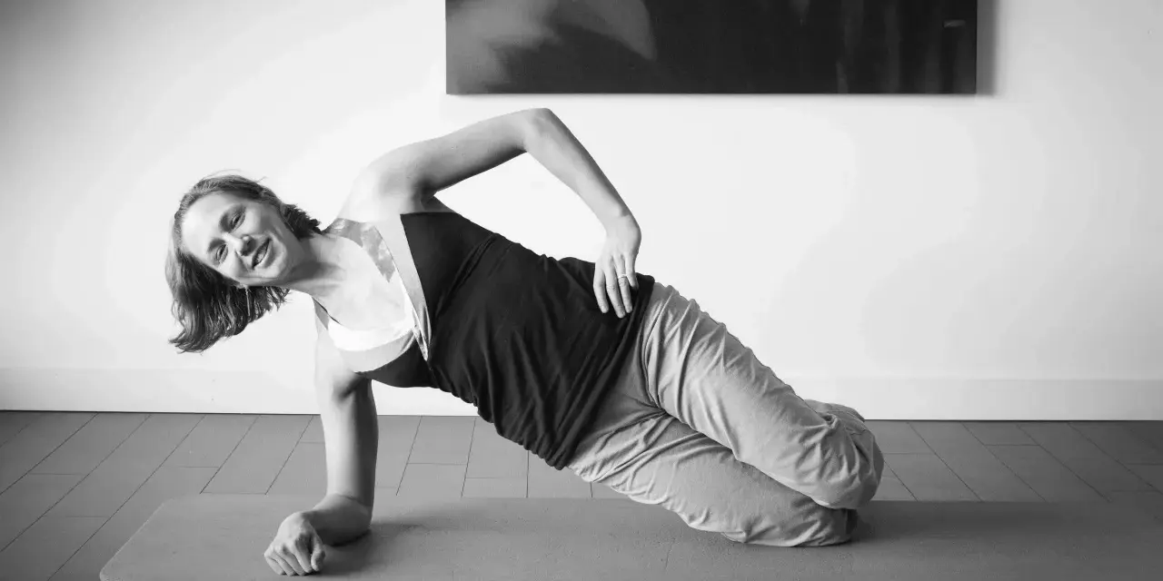 Femme souriante en plein gainage latéral sur un tapis de yoga.