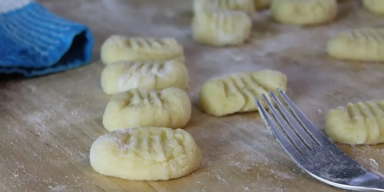 Frisch geformte Gnocchi liegen auf bemehltem Holz. Eine Gabel und ein blauer Lappen deuten auf die Zubereitung von Gnocchi Rezepten hin.