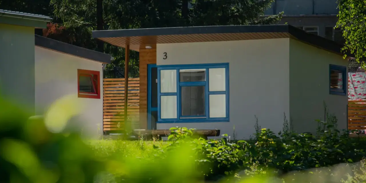 Nowoczesne domki letniskowe w osadzie Chmielaki. Jasne ściany, niebieskie okna i drewniane elementy tworzą przytulną atmosferę.