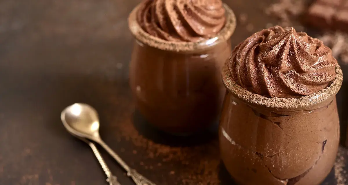 Deux pots de mousse au chocolat onctueuse, saupoudrés de cacao, avec deux cuillères argentées.