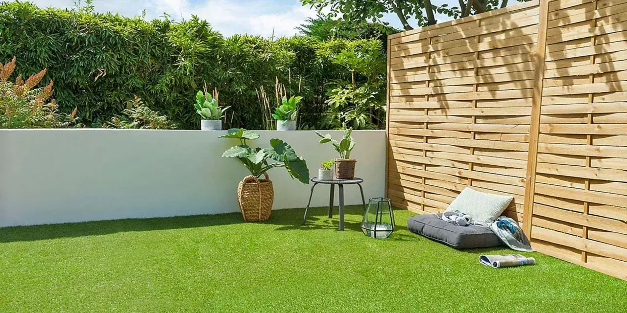 Terraza con césped artificial verde vibrante, plantas en macetas, un banco y una valla de madera.