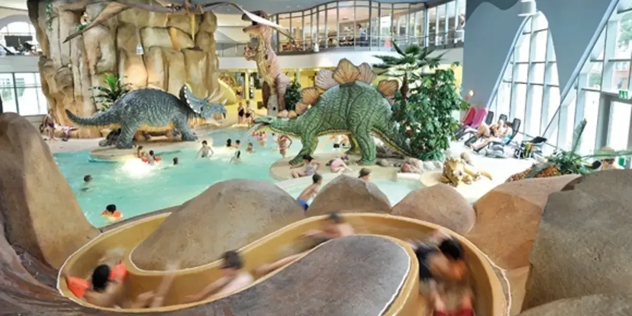 Kinder planschen im Dino-Bad, ein perfektes Ziel für die Herbstferien in Hamburg. Rutschen und Dinosaurier sorgen für Spaß.