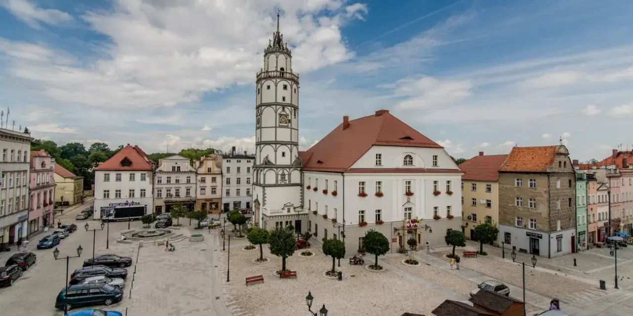 Rynek w Paczkowie, polskie Carcassonne, z ratuszem i wieżą. Brukowany plac, samochody, ławki i małe drewniane budki.