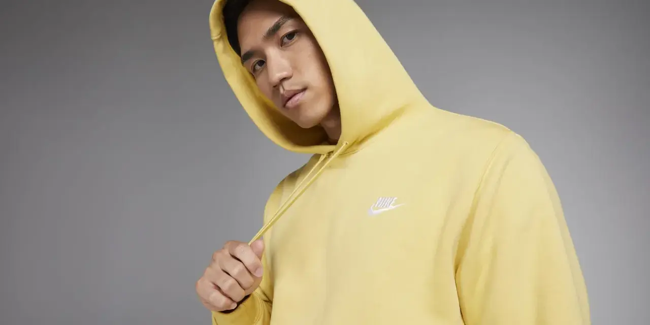 Młody mężczyzna w żółtej bluzie z kapturem Nike Club.