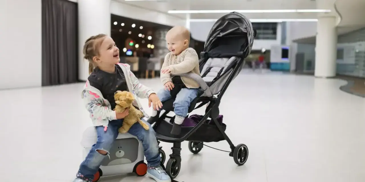 Dzieci w podróży z Ryanair. Starsza siostra siedzi na walizce z misiem, młodsza w wózku.