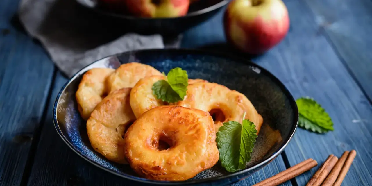 Délicieux beignets aux pommes dorés, garnis de menthe fraîche et accompagnés de bâtons de cannelle sur une table en bois bleu.