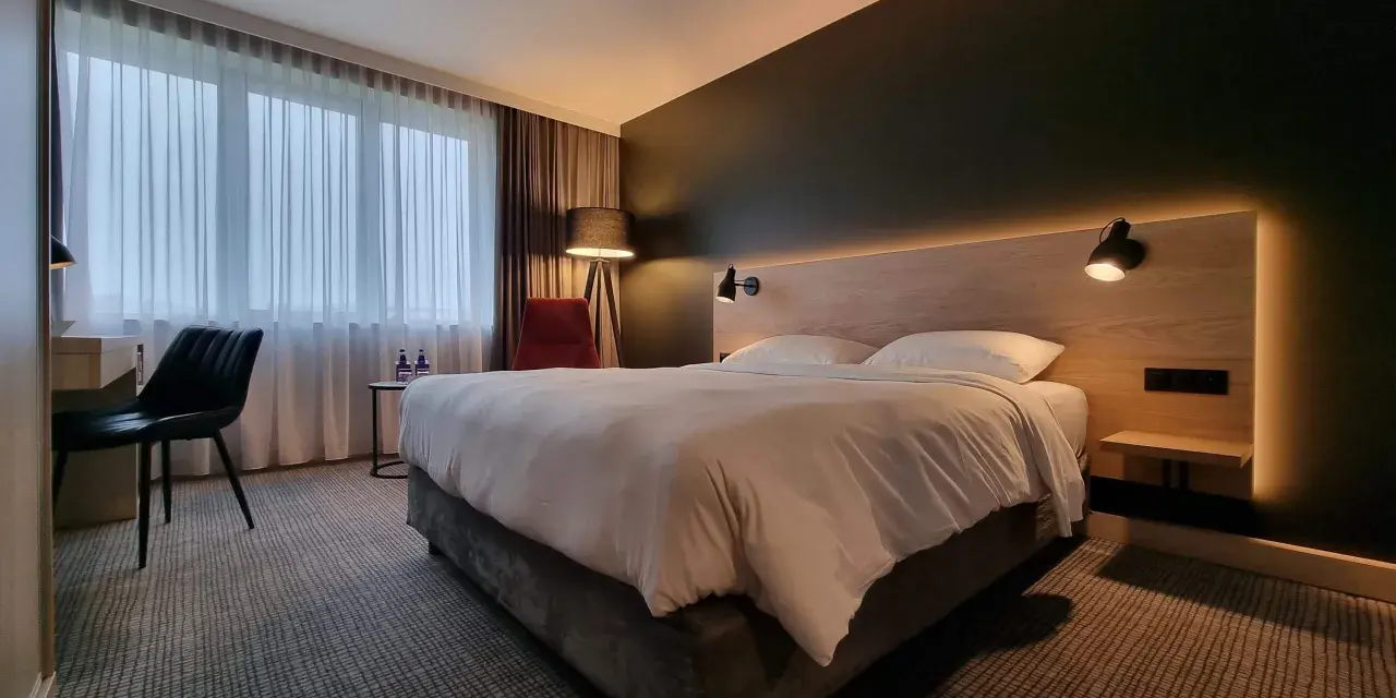 Przytulny pokój w Park Inn Papenburg: wygodne łóżko, designerskie lampy i okna z zasłonami.