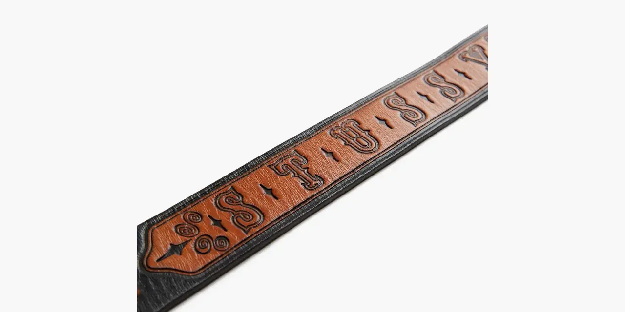 Cintura in pelle marrone con logo Stussy inciso e dettagli decorativi.