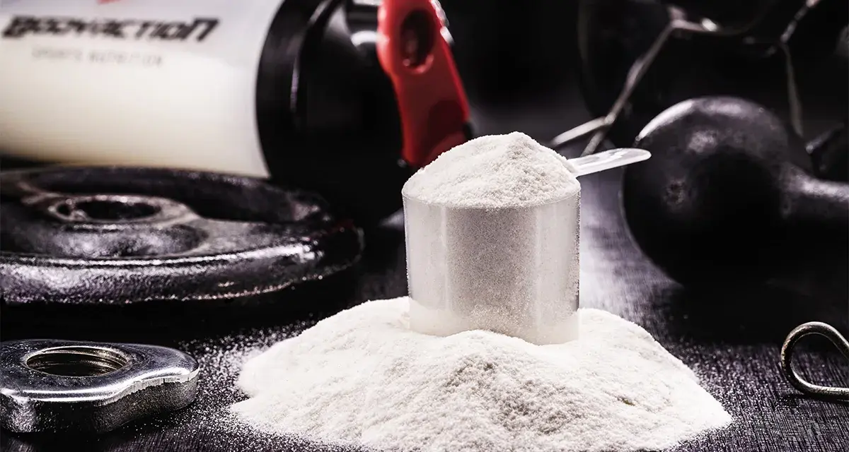 Polvo blanco en una cuchara medidora, junto a pesas y un bote de suplemento. Descubre para qué sirve la creatina y potencia tus entrenamientos.