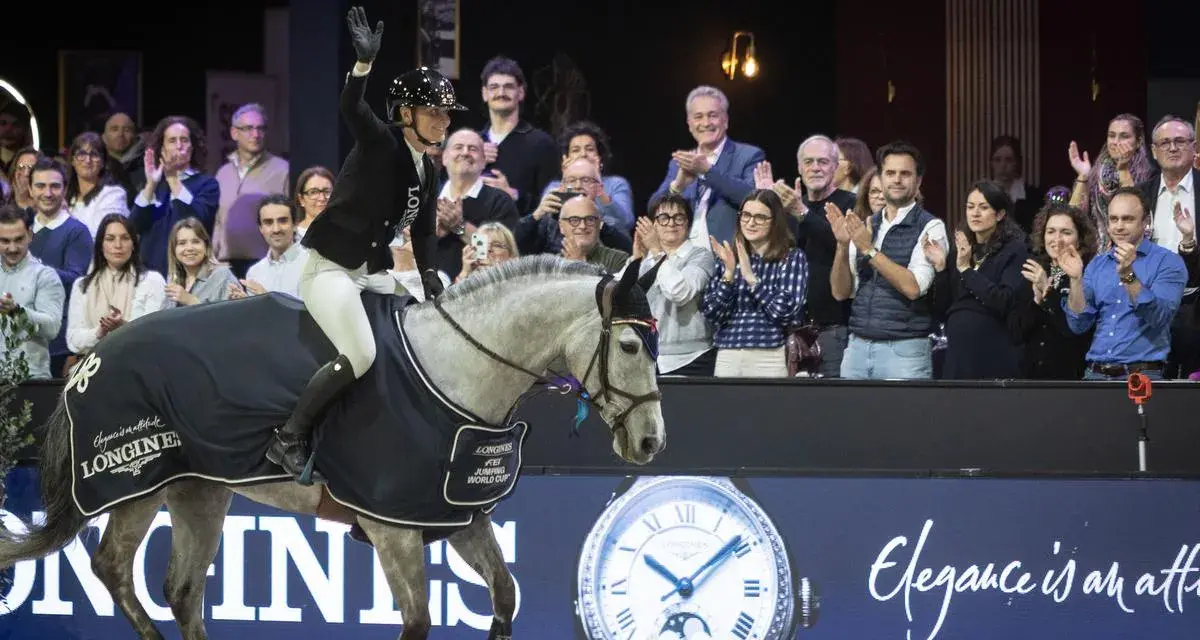 Cavalier(e) saluant la foule, son cheval gris couvert d'une cape aux couleurs de la Longines FEI Jumping World Cup.