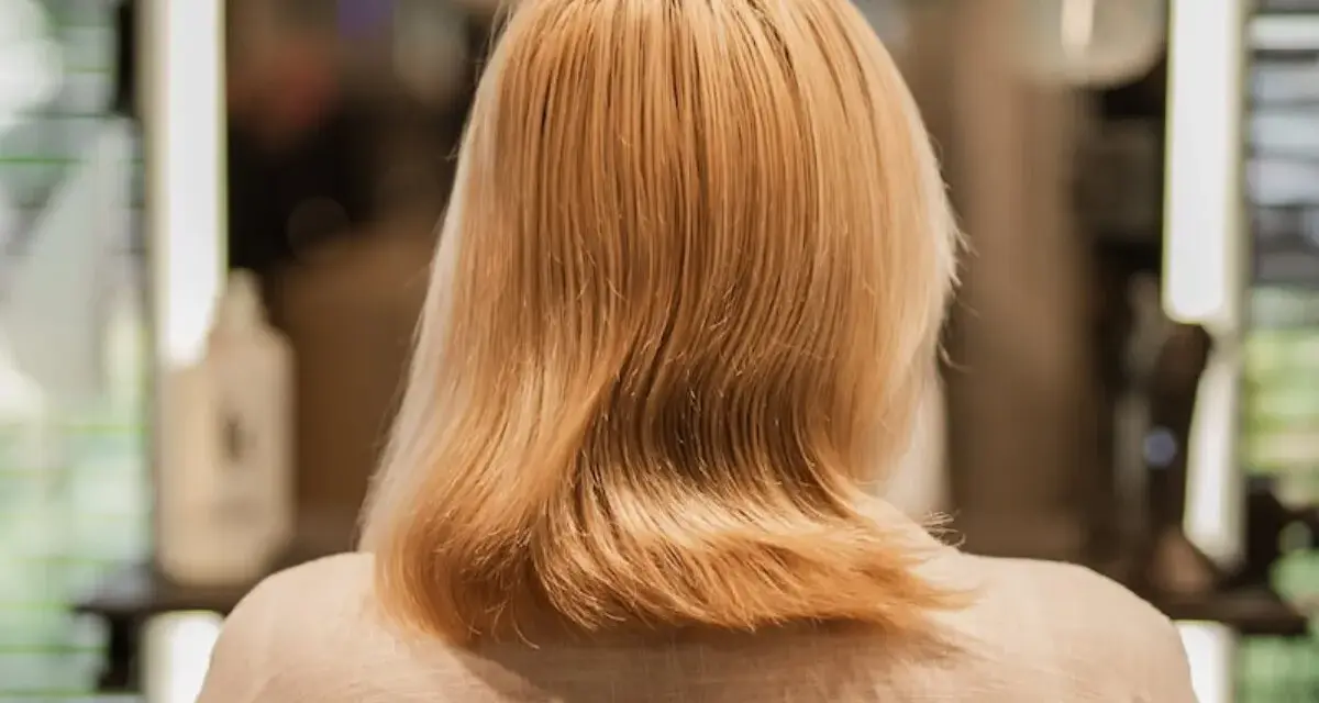 Kobieta z blond włosami, zastanawia się, jak nosić siwe włosy. Włosy są średniej długości, lekko falowane.