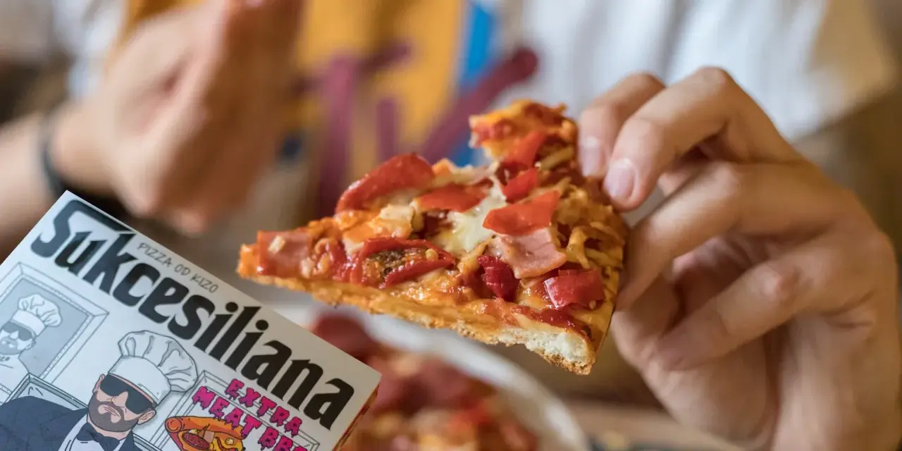Kawałek pysznej pizzy od Kizo, z dodatkami mięsnymi i papryką, na opakowaniu widnieje napis "Sukcesiliana Extra Meat BBQ".