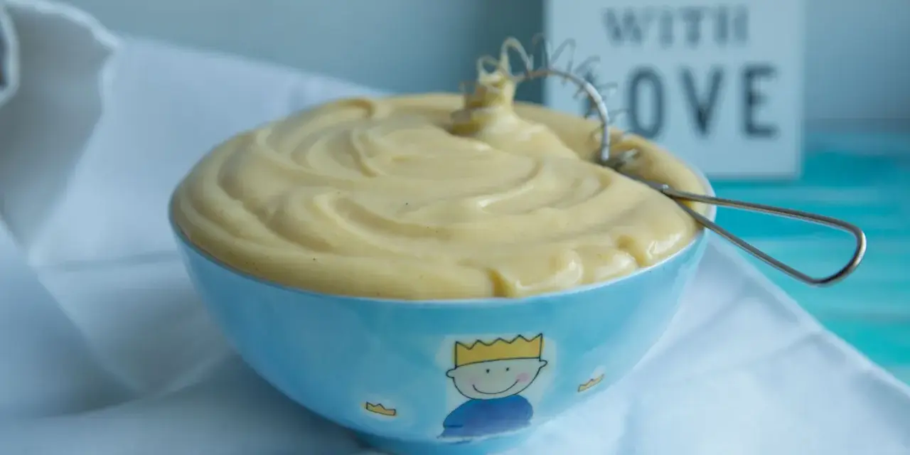 Gładki, kremowy krem patissiere w niebieskiej miseczce z małym królem. Idealny do deserów.