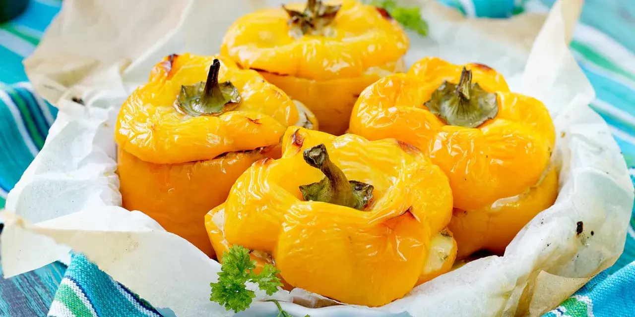 Quatre poivrons farcis jaunes, dorés et appétissants, servis dans un plat garni de papier sulfurisé et décorés de persil frais.