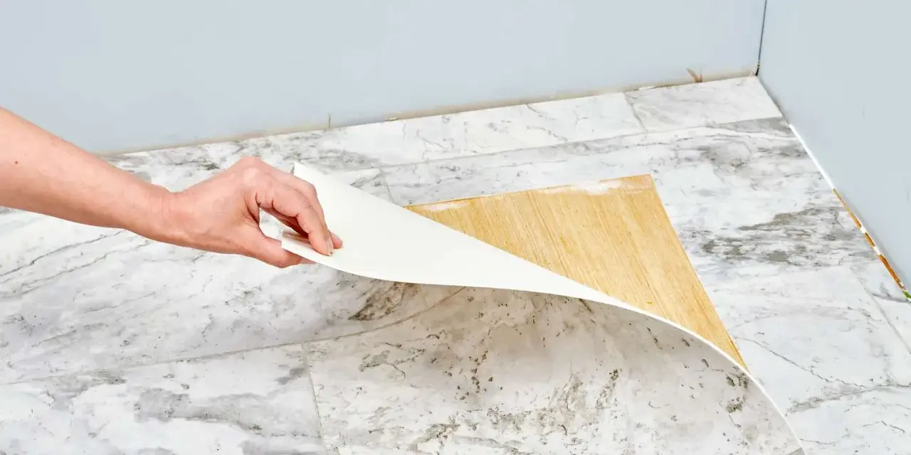 Mano retirando capa de vinilo del suelo. Un paso clave para saber como quitar pintura de caucho del suelo.