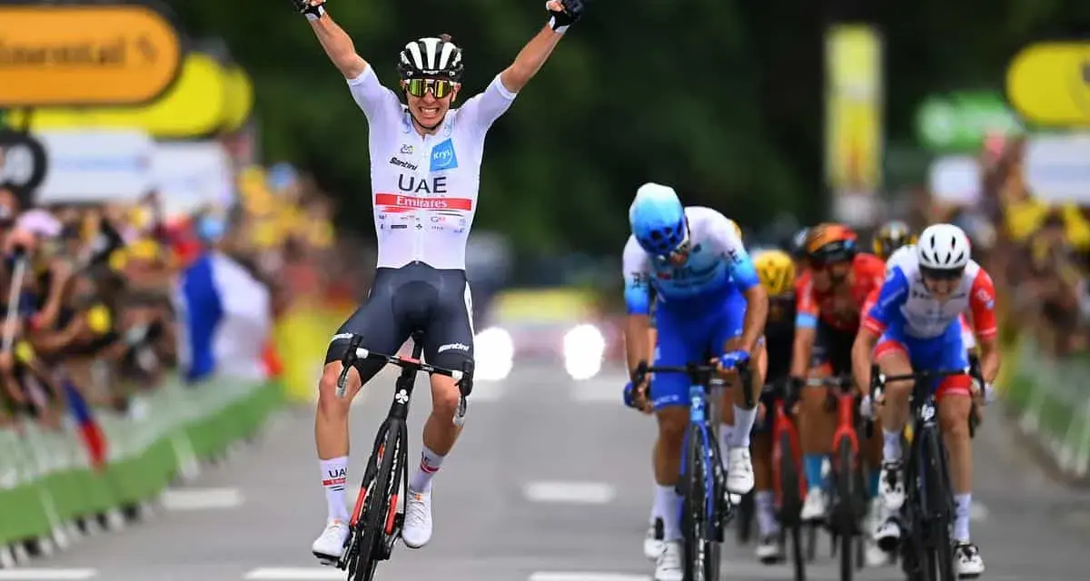 A cyclist in a white UAE Emirates jersey celebrates victory at the Tour de France, arms raised in triumph as he crosses the finish line.