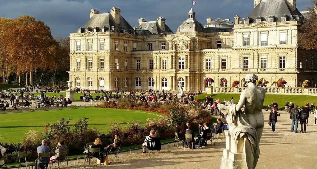 Palacio de Luxemburgo y su jardín con gente sentada y un monumento.