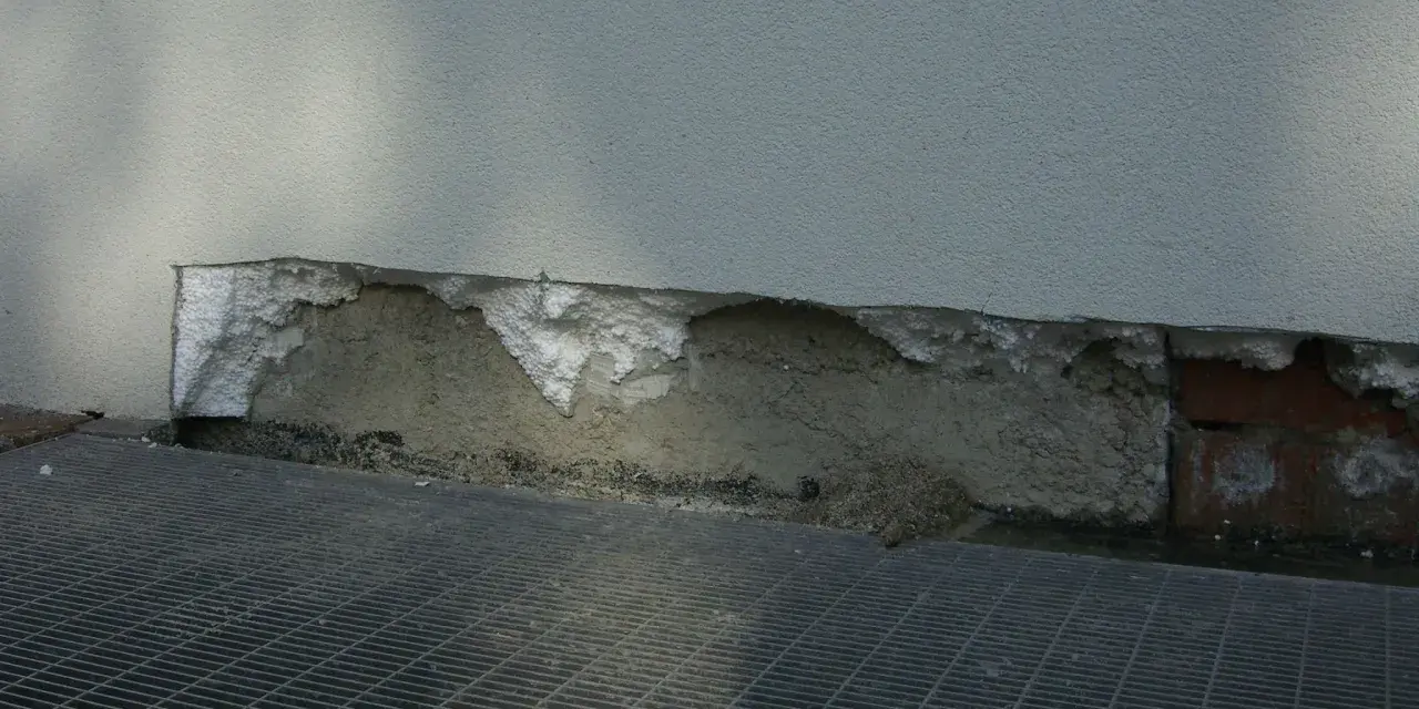 Dettaglio di un muro con isolamento danneggiato, mostrando la differenza tra polistirolo e polistirene espanso.