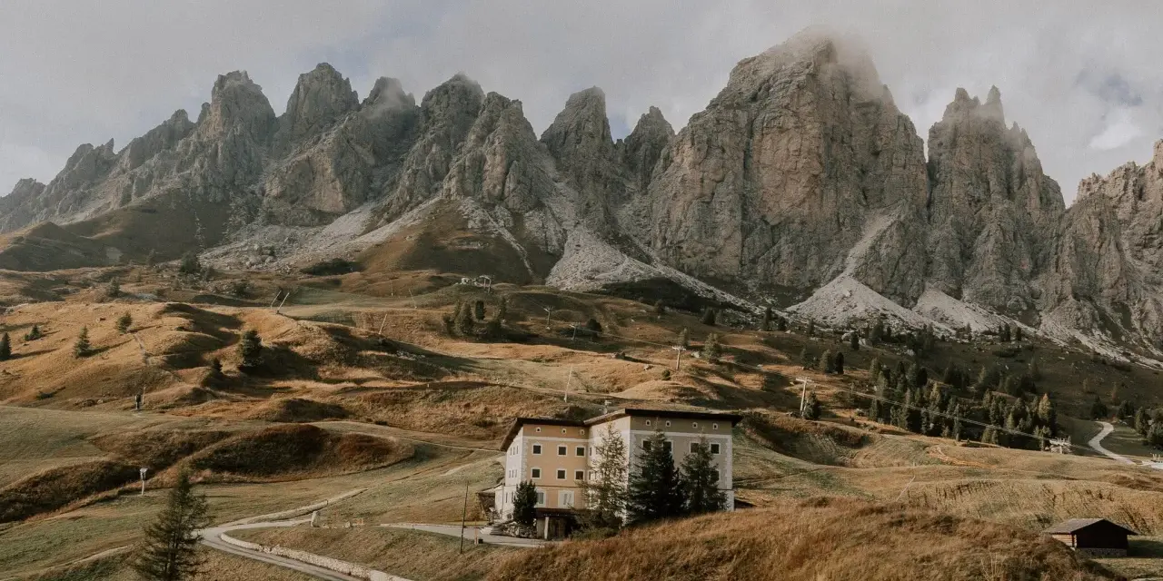 Malownicze **Val di Funes** z górami w tle, hotel na wzgórzu i kręta droga.