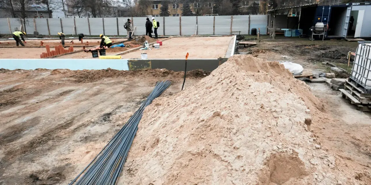 Budowa w marcu 2026. Działka z uregulowanym stanem prawnym, przygotowana pod fundamenty. Piasek, zbrojenie i pracownicy na placu budowy.