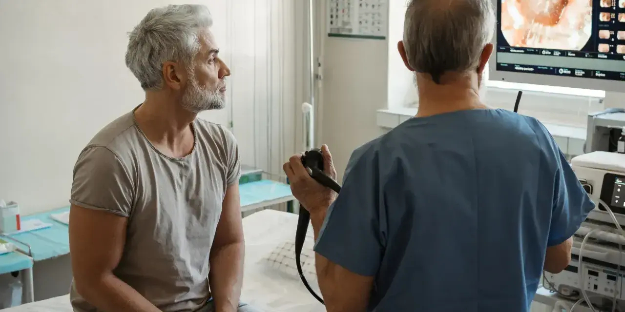 Lekarz wykonuje rektoskopię u pacjenta, obserwując obraz na monitorze.