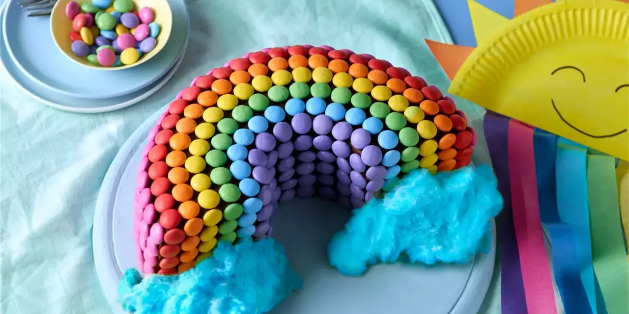 Bunter regenbogen kuchen, verziert mit vielen bunten Smarties und blauer Zuckerwatte als Wolken. Ein Fest für die Augen!