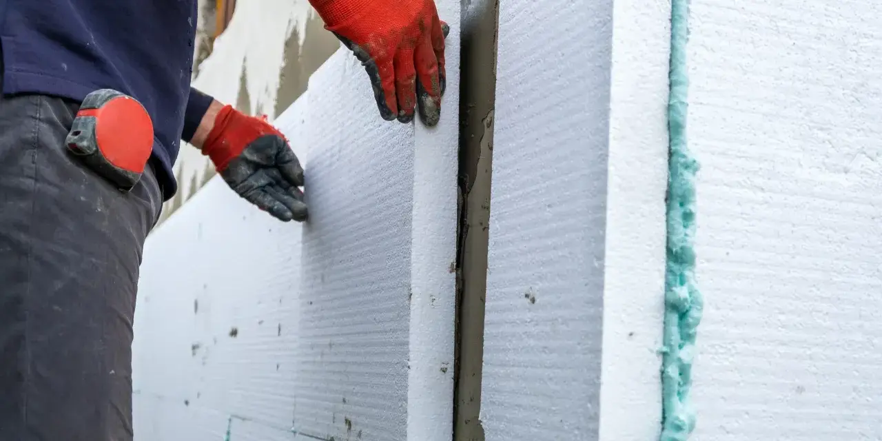 Operaio posa pannelli isolanti per cappotto termico, attenzione alle fughe e alle soglie per evitare ponti termici.