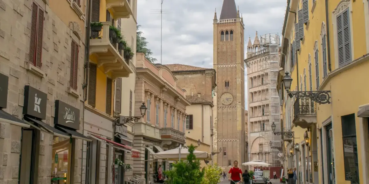 A man cycles down a street in Parma, Italy, with a tall clock tower in the background. This view captures the essence of a journey from Bologna to Parma.